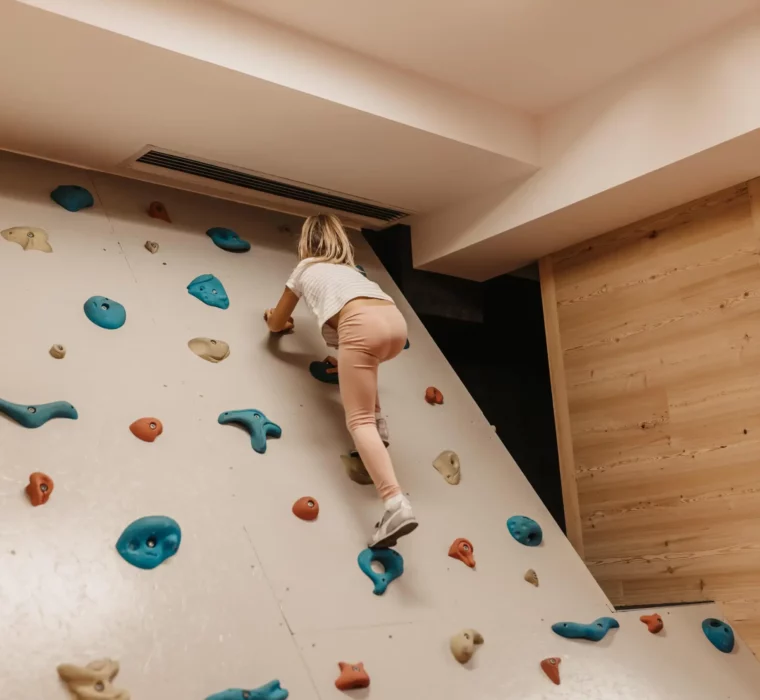 A small child bravely scales the indoor climbing wall at Hofgut Wagrain - full of energy, the joy of discovery and childlike pride.