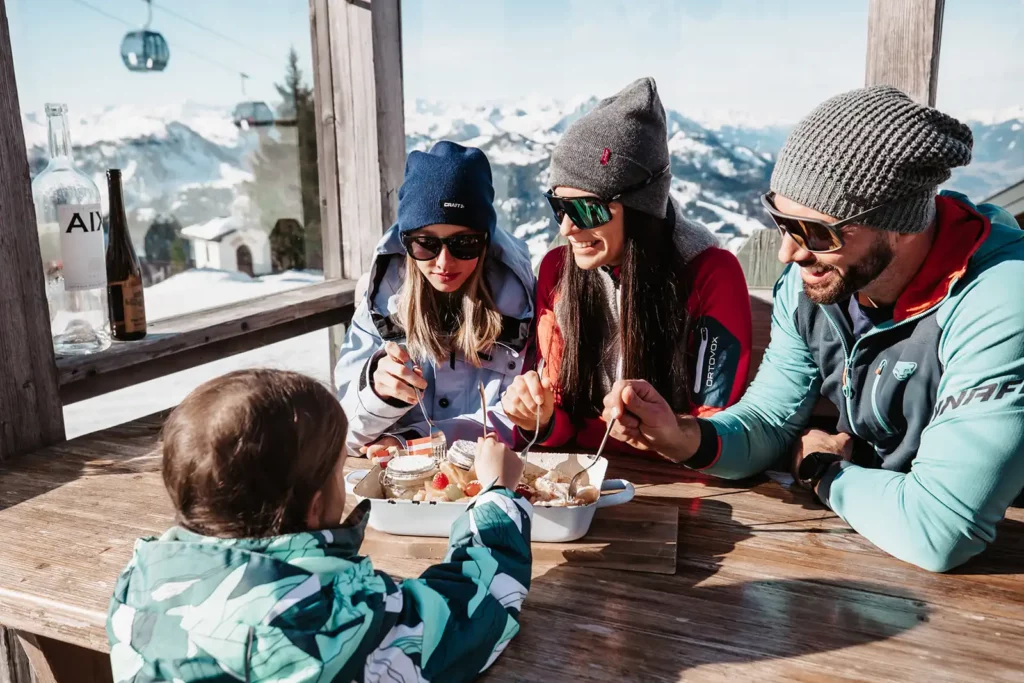 Familien nyder Kaiserschmarrn i en skihytte med udsigt over bjergene.