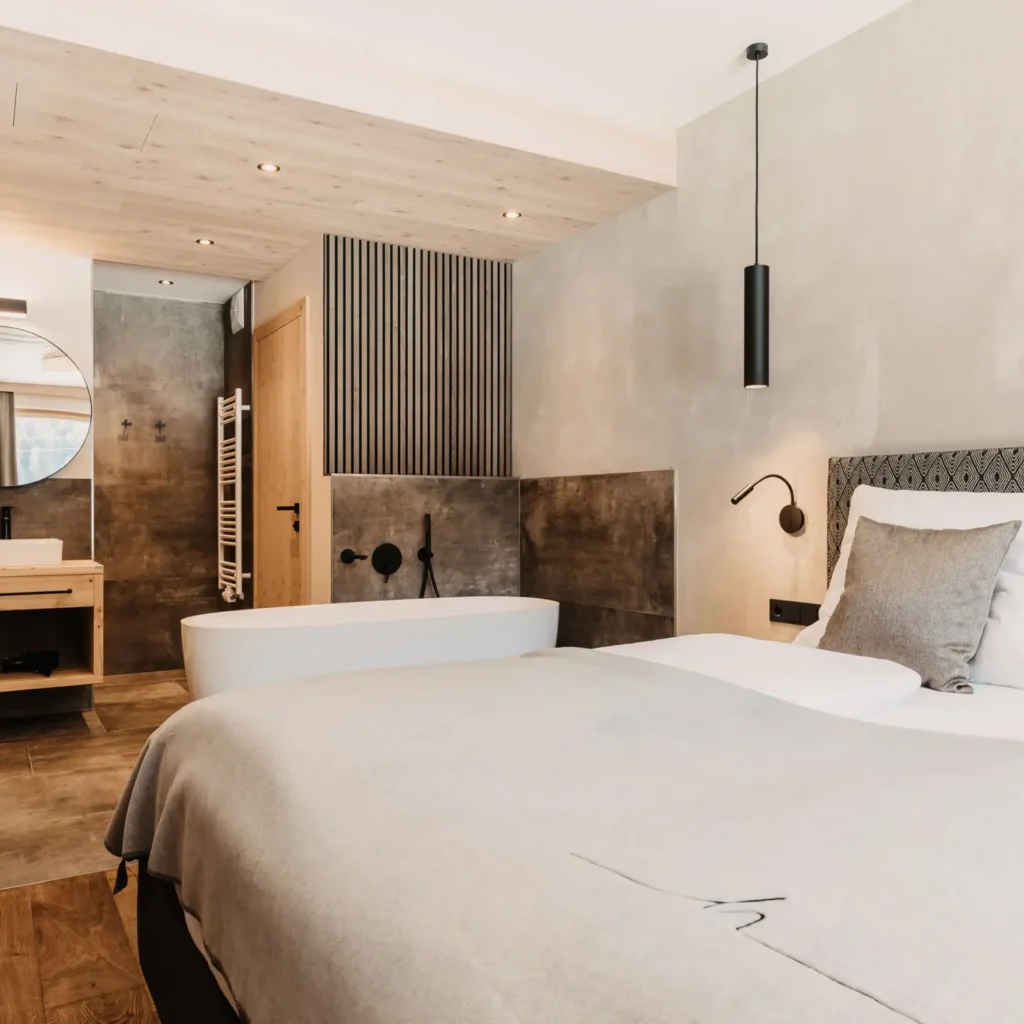 hofgut-apartment-lifestyle-resort-schlafraum-65 Helles Schlafzimmer im Hofgut Wagrain mit gemütlichem Doppelbett und offenem Bad mit freistehender Wanne.