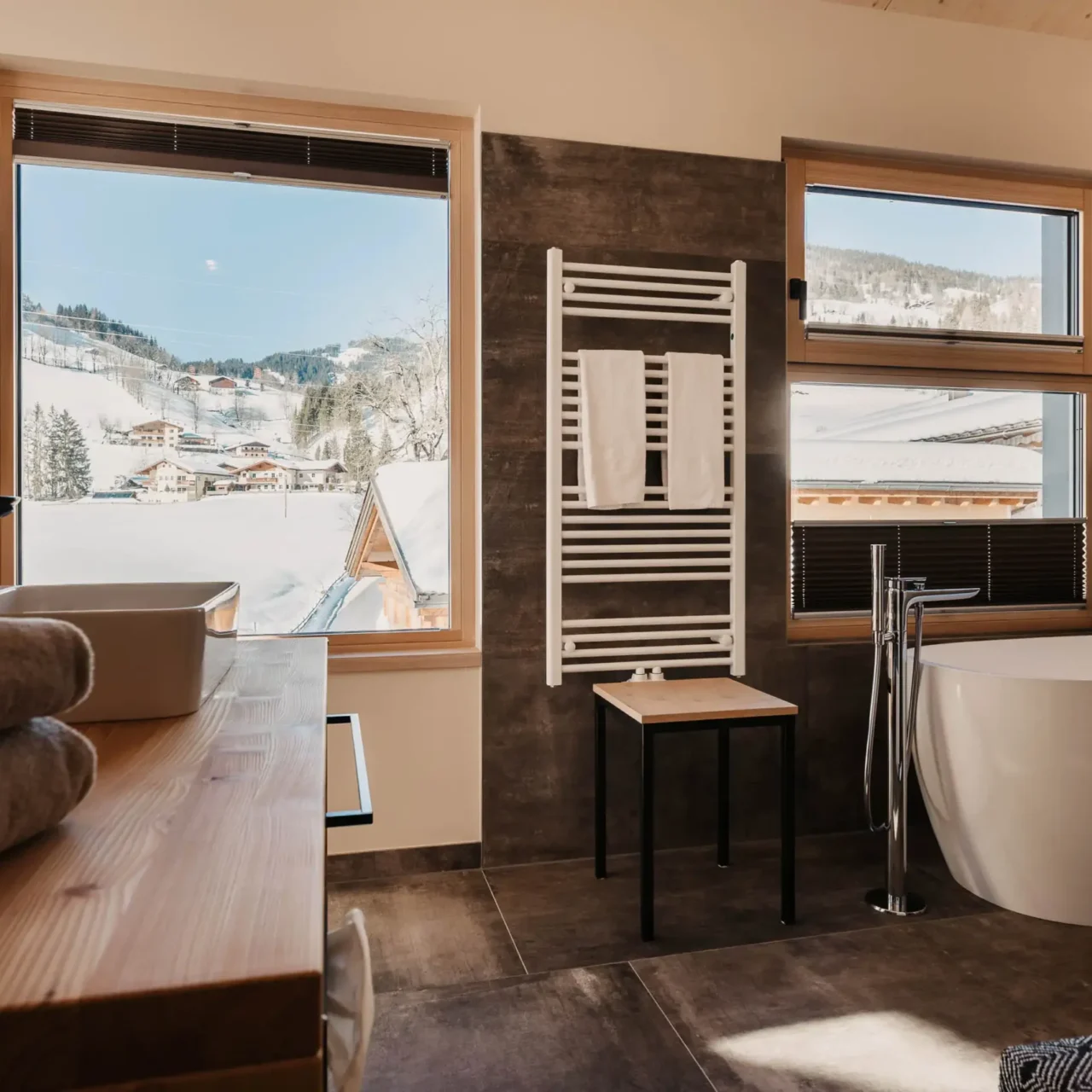 Modernes Badezimmer im Hofgut Wagrain mit freistehender Badewanne und Ausblick auf die verschneite Winterlandschaft der Salzburger Alpen.