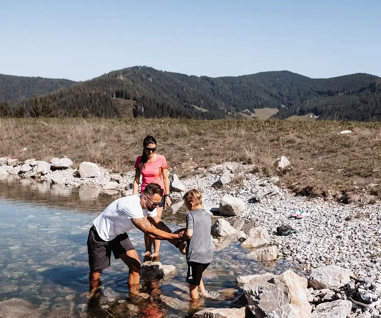 Familie genießt barfuß das klare, kühle Wasser eines alpinen Baches - Naturerlebnis für Groß und Klein.