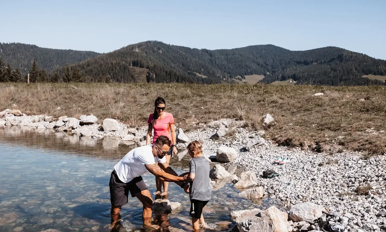 Familie genießt barfuß das klare, kühle Wasser eines alpinen Baches - Naturerlebnis für Groß und Klein.