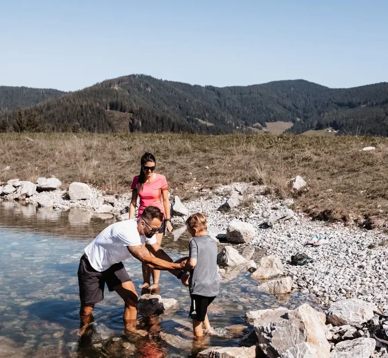 Familie genießt barfuß das klare, kühle Wasser eines alpinen Baches - Naturerlebnis für Groß und Klein.