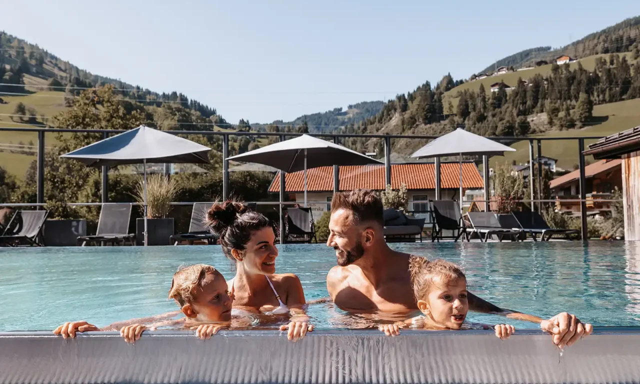 Glückliche Familie entspannt im Rooftopool des Hofgut Wagrain mit Panoramablick auf die Berge.