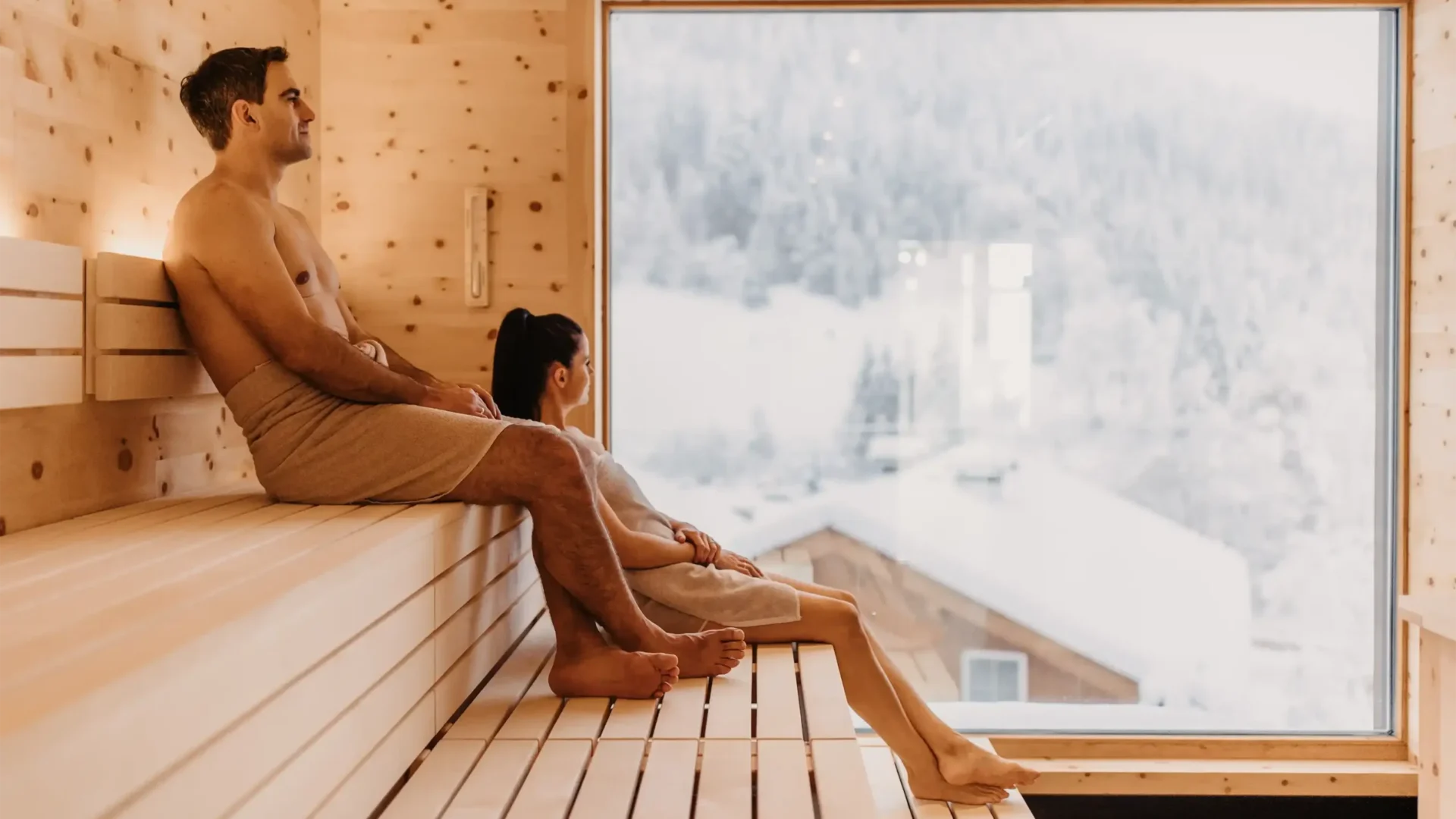 09-12-2021_SelinaFlaschPhotography-230-Sauna-3000x2000 Wohlfühlmoment mit Panoramablick: Ein Paar genießt die wohltuende Wärme der Skysauna im Hofgut Wagrain mit Blick auf die verschneiten Dächer der alpinen Winterlandschaft.