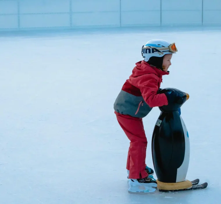Ein Kind läuft auf einer Eisfläche am Eislaufplatz Wagrain und hält sich an einer Pinguin-Laufhilfe fest.
