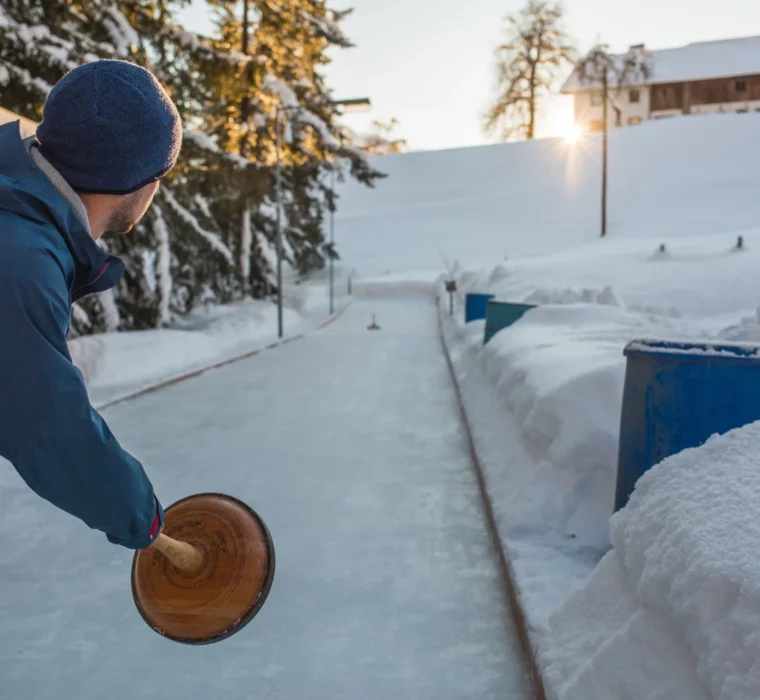 Tradition meets winter fun – curling amidst snow-covered mountain scenery at sunset.