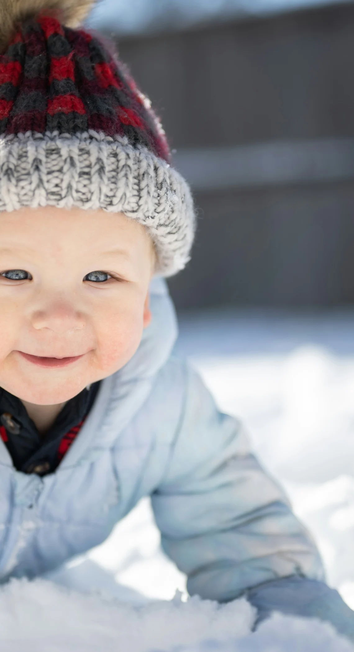 Ein lächelndes Kleinkind in Winterkleidung spielt im frischen Schnee.
