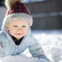 Ein lächelndes Kleinkind in Winterkleidung spielt im frischen Schnee.