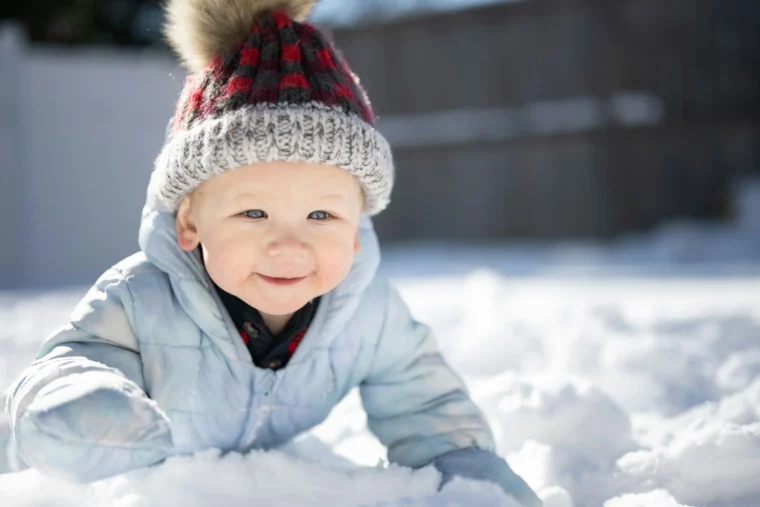 Ein lächelndes Kleinkind in Winterkleidung spielt im frischen Schnee.