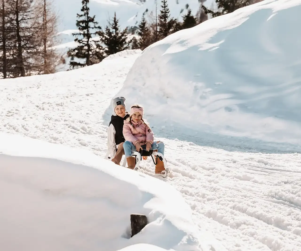 Two children on a sleigh, laughing, in winter clothes on a snowy slope.