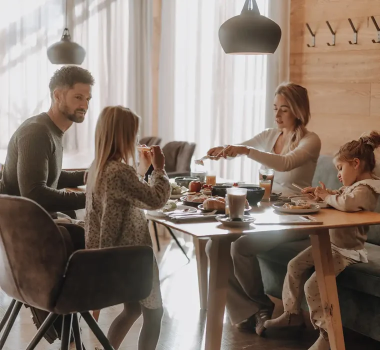 La famiglia di quattro siede al tavolo della colazione presso la colazione dell'esperto nella Hofgut Wagrain-Restaurant vaMoos.