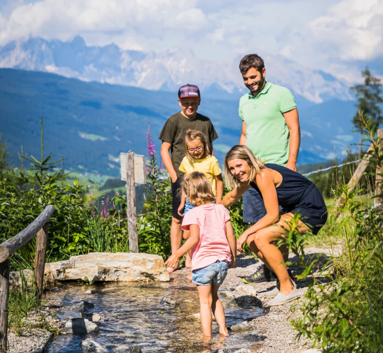 Familie mit Kindern entdeckt einen Natur-Wasserspielbereich entlang eines Wanderwegs im Salzburger Land