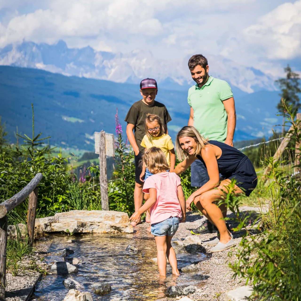 Familie mit Kindern entdeckt einen Natur-Wasserspielbereich entlang eines Wanderwegs im Salzburger Land