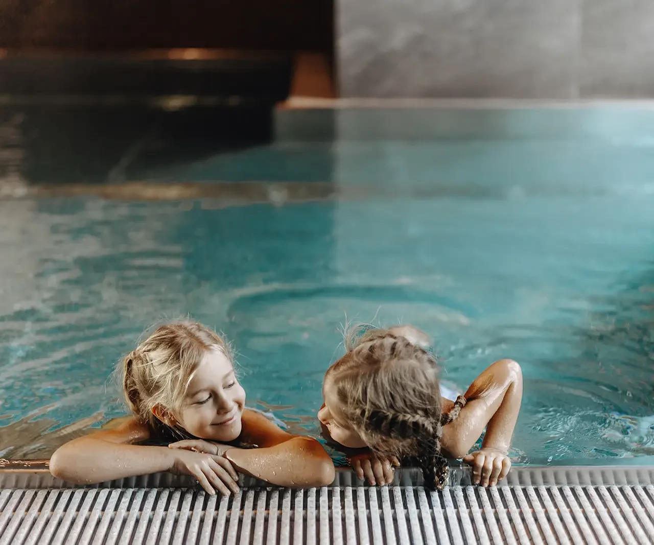 Zwei Kinder stützen sich im Hallenbad am Beckenrand im Hofgut Wagrain ab.