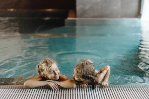 Zwei Kinder stützen sich im Hallenbad am Beckenrand im Hofgut Wagrain ab.