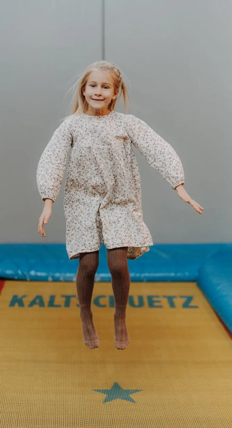 Dítě skáče vysoko na trampolíně v krytém herním světě Hofgut Wagrain.